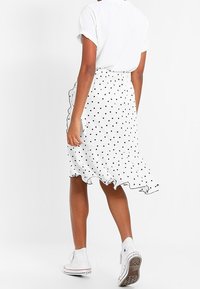 Vit kjol med prickar och volang i nederkant, tillverkad av lätt tyg. Bärs med en kortärmad vit skjorta och vita sneakers.