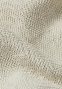 Jasnobeżowa tkanina o teksturowanej powierzchni z wplecionym wzorem, charakteryzująca się miękkim, lekko szorstkim uczuciem oraz subtelnymi odcieniami kolorów.