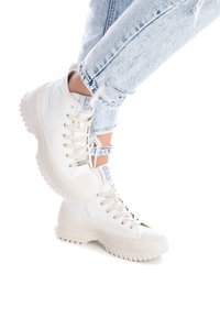 Zapatillas altas en lona color blanco roto con suela de goma texturizada. Incluyen características como puntera redonda, costuras reforzadas y un diseño de cordones.