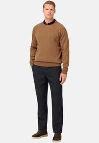 Rudas megztinis su lygiu apvadu, derinamas su mėlynomis kelnėmis ir rudais zomšiniais batais. Apranga pasižymi kasdienišku, sluoksniuotu stiliumi.