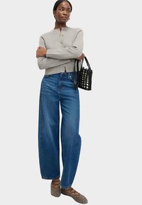 Grå texturerad cardigan med rund hals och guldfärgade knappar, kombinerad med blå, högmidjade jeans. Svart vävd handväska och mönstrade ballerinaskor.