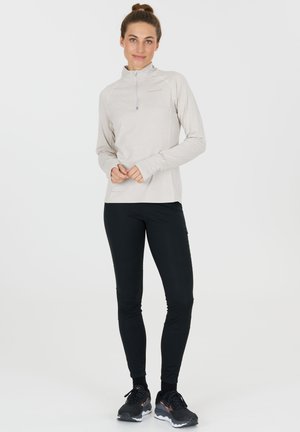 Lys beige langærmet top med halv-lynlås og tommelfingerhuller, parret med sorte tætsiddende bukser. Har en glat tekstur og atletisk design.
