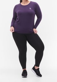 Langsleeve paarse top met ronde halslijn, zwarte leggings en zwarte sport schoenen. Bevat een klein logo op de borst.
