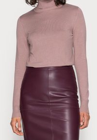 Maglione a collo alto in maglia di colore rosa chiaro con maniche lunghe. Abbinato a una gonna a tubino in pelle di un profondo bordeaux, aderente e con dettagli delle cuciture visibili.
