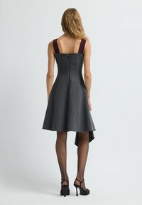 Graues A-Linien-Kleid mit kastanienbraunen Trägern, Reißverschluss und asymmetrischem Saum. Tragend mit schwarzen hohen Sandalen und transparenten schwarzen Strumpfhosen.