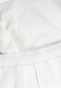 Vit ribbad tyg med en strukturerad yta, som har ett elastiskt midjeband och lätt rynkning, vilket betonar mjukhet och stretch.
