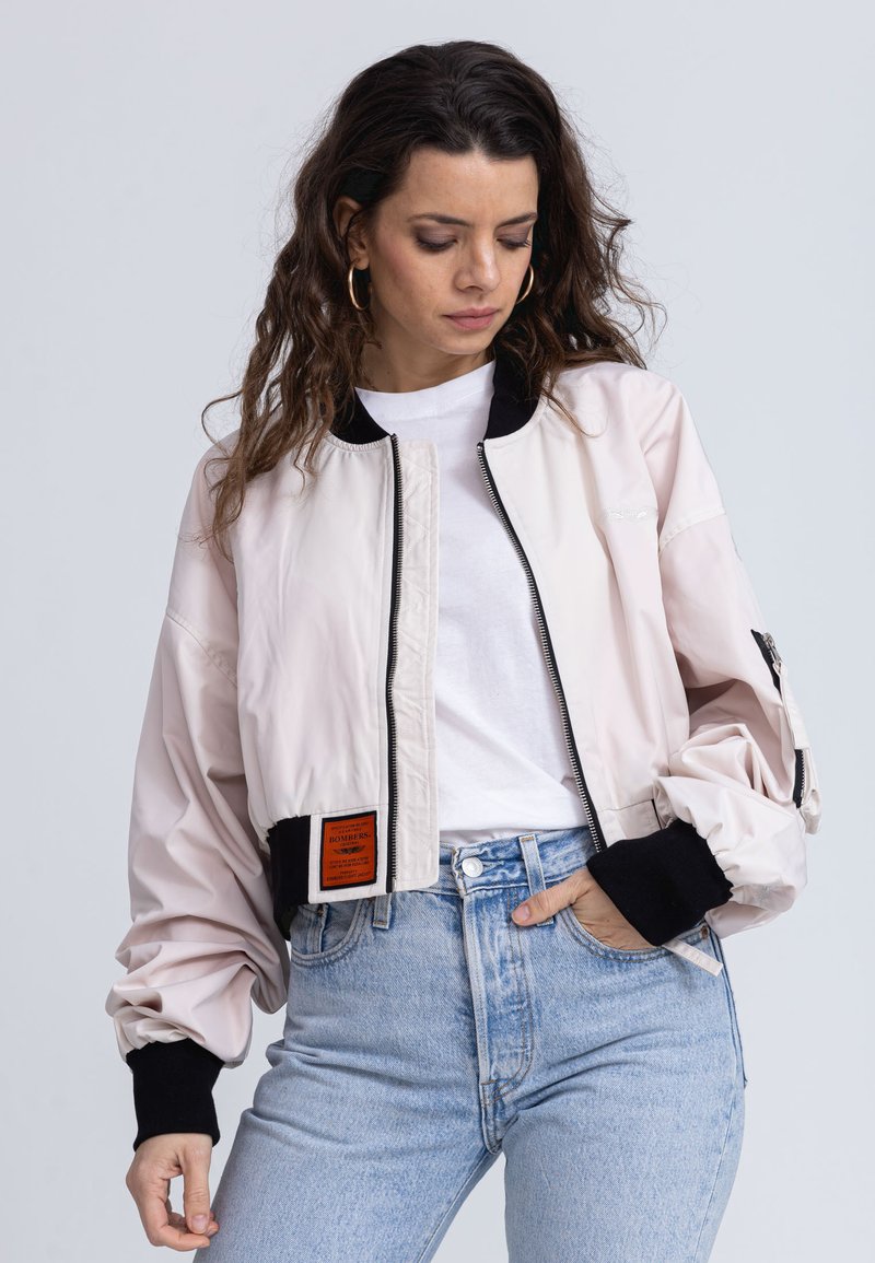 Helle rosa Bomberjacke mit einem schwarzen gerippten Kragen und Bündchen. Sie zeigt einen Frontreißverschluss, Taschen an den Seiten und ein orangenes Markenlabel am Saum.