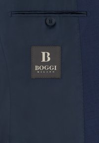 Intérieur de veste bleu foncé avec une étiquette indiquant "B BOGGI MILANO" sous un bouton unique et une poche intérieure horizontale.