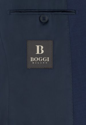 Interior de chaqueta azul oscuro con una etiqueta que dice "B BOGGI MILANO" bajo un único botón y un bolsillo interior horizontal.