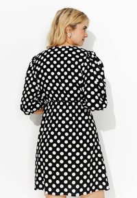 Robe noire avec de grands pois blancs, manches courtes bouffantes, taille cintrée et jupe fluide, fabriquée dans un tissu lisse et léger.