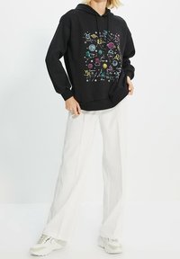 Sweat à capuche noir avec un motif graphique de signes astrologiques et d'éléments célestes en encre colorée. Doté d'une capuche avec cordon de serrage et de poignets côtelés.