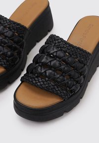 Sandalias de cuña negras con parte superior de cuero trenzado, diseño de punta abierta y plantilla acolchada en tono bronce sobre una suela de plataforma negra texturizada.