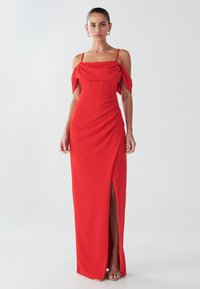 Rotes, bodenlanges Kleid aus glattem Stoff mit schulterfreien Ärmeln, drapierten Details und einem hohen Schlitz am Oberschenkel.