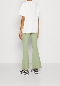 Vit t-shirt med kort ärm, ljusgröna ribbade utsvängda byxor och svarta sneakers med vita detaljer. Enkel, vardaglig outfit.