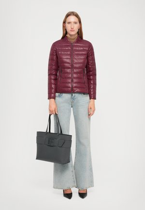 Giacca a vento marsala con un design aderente, tasche con zip, imbottitura leggera e colletto alto, abbinata a jeans in denim a gamba larga e una borsa a tracolla nera.