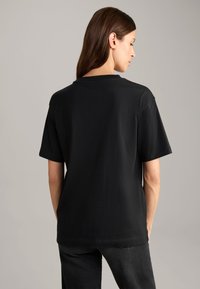 Zwarte katoenen T-shirt met korte mouwen en een ronde hals. De achterkant is eenvoudig met een relaxte pasvorm, heeft een soepele textuur en geen zichtbare logo's.