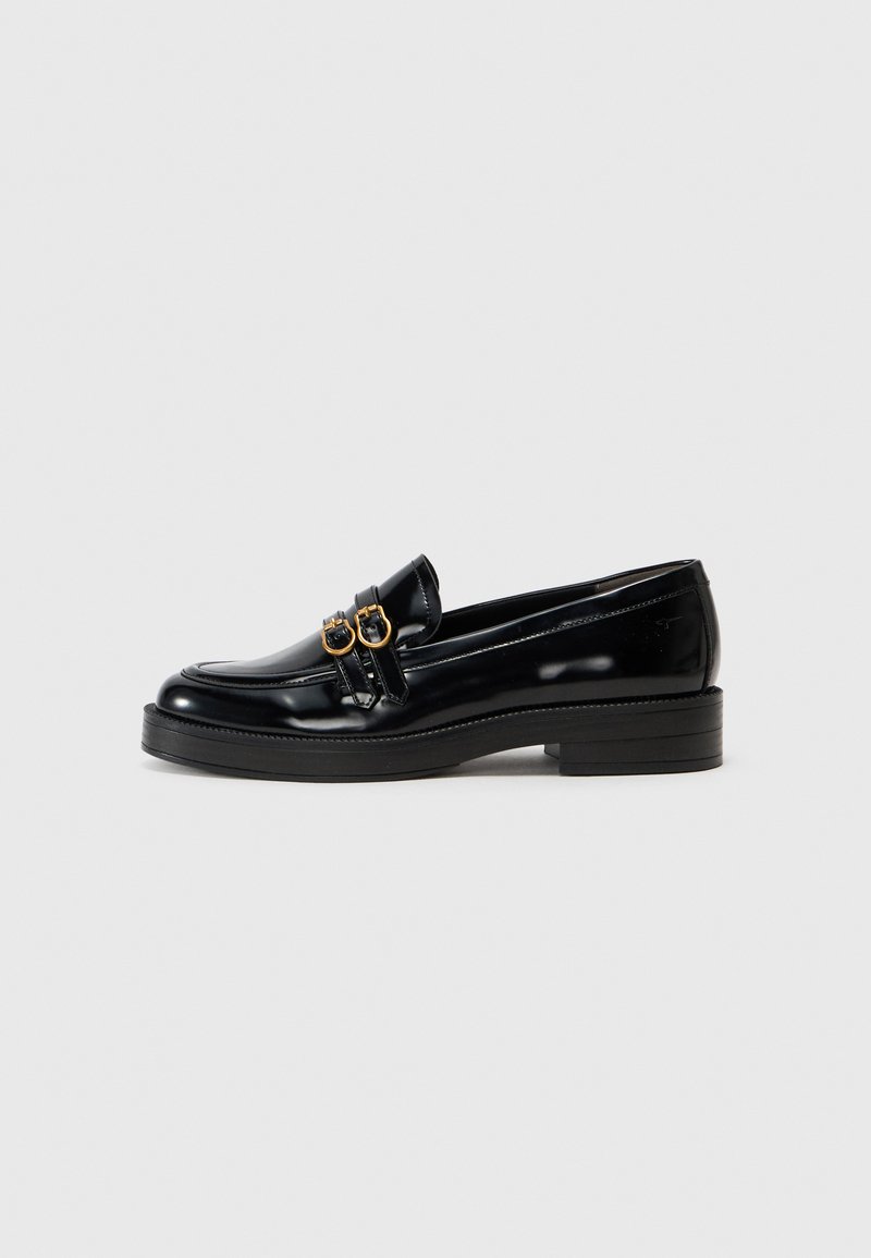 Schwarze Lackleder-Loafer mit abgerundetem Zeh, ausgestattet mit zwei goldfarbenen Schnallen und einer dicken schwarzen Gummisohle.