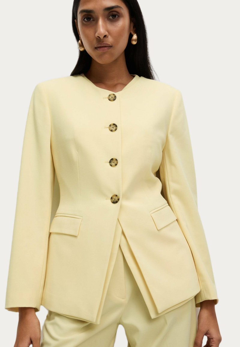 Yellow blazer with a structured design, featuring a V-neck, five rounded buttons, and two front pockets. Smooth, tailored fabric, long sleeves.