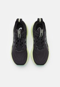 Zapatos deportivos negros con parte superior de malla transpirable, suela verde lima y acentos reflectantes. Cuenta con un diseño de cordones y un collar acolchado.