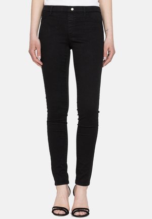 Czarne czarne jeansy slim fit noszone przez stojącą osobę, zestawione z czarnymi sandałami na wysokim obcasie z odkrytymi palcami i białą bluzką.