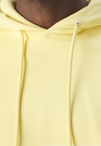 Felpa con cappuccio giallo chiaro realizzata in tessuto morbido, dotata di coulisse con accessori in argento e logo del marchio "SANDRO" in rilievo sul davanti.