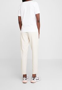 Biała bawełniana koszulka z krótkim rękawem, zestawiona z jasnobeżowymi spodniami i wielokolorowymi sneakersami z czarnymi akcentami i białą podeszwą.