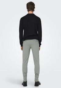 Maglione lavorato a maglia nero con scollo rotondo abbinato a pantaloni fitted grigio chiaro, che mostrano una texture liscia e dettagli sui taschini discreti.