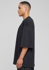 Čierne oversized tričko s krátkym rukávom vyrobené z bavlny, s okrúhlym výstrihom a voľným strihom, viditeľné švy pozdĺž švov.