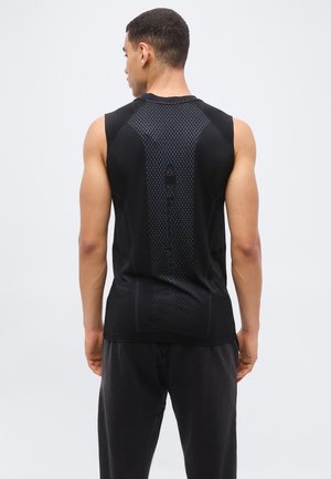 Férfi hátrafelé nézve, fekete, ujjatlan sportpólót visel, amely középen a hátán texturált függőleges csíkkal és logóval rendelkezik.