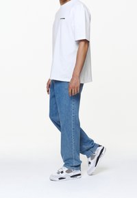 Bílá bavlněná tričko s černým textem, modré džínové kalhoty a černo-bílé tenisky s síťovinovými detaily. Casual střih s minimálním designem.