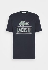 Navy blue short-sleeve t-shirt with green and white Lacoste crocodile logo and "LACOSTE" text centered on the front.