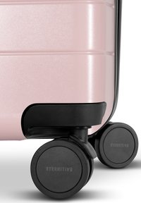 Hard-shell suitcase in glossy light pink with black accents. Features four smooth, multi-directional wheels for easy mobility.
