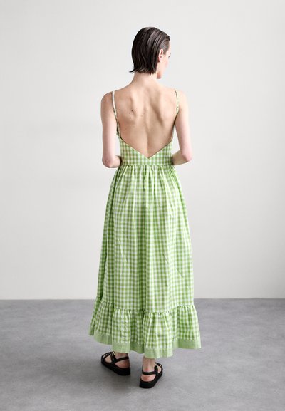 Groene geruite maxi-jurk met een lage V-hals aan de achterkant, verstelbare dunne bandjes en een gerimpelde zoom. Draag het met zwarte sandalen.