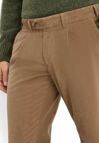 Pantaloni in velluto a coste marrone con una superficie testurizzata, dotati di chiusura con bottone, tasche laterali e vestibilità su misura.