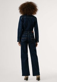 Mörk denimjacka och högmidjade jeans med rak bendesign. Har en brun läderlapp på baksidan och kontrasterande sömmar.