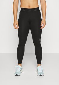 Leggings negros con una cintura alta que presentan acentos texturizados y un ajuste elegante. Llevadas con zapatillas deportivas de color azul claro.