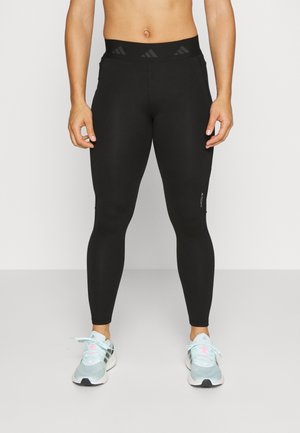 Czarne legginsy z wysokim stanem, z teksturalnymi akcentami i dopasowanym krojem. Na nogach lekkie, niebieskie buty sportowe.