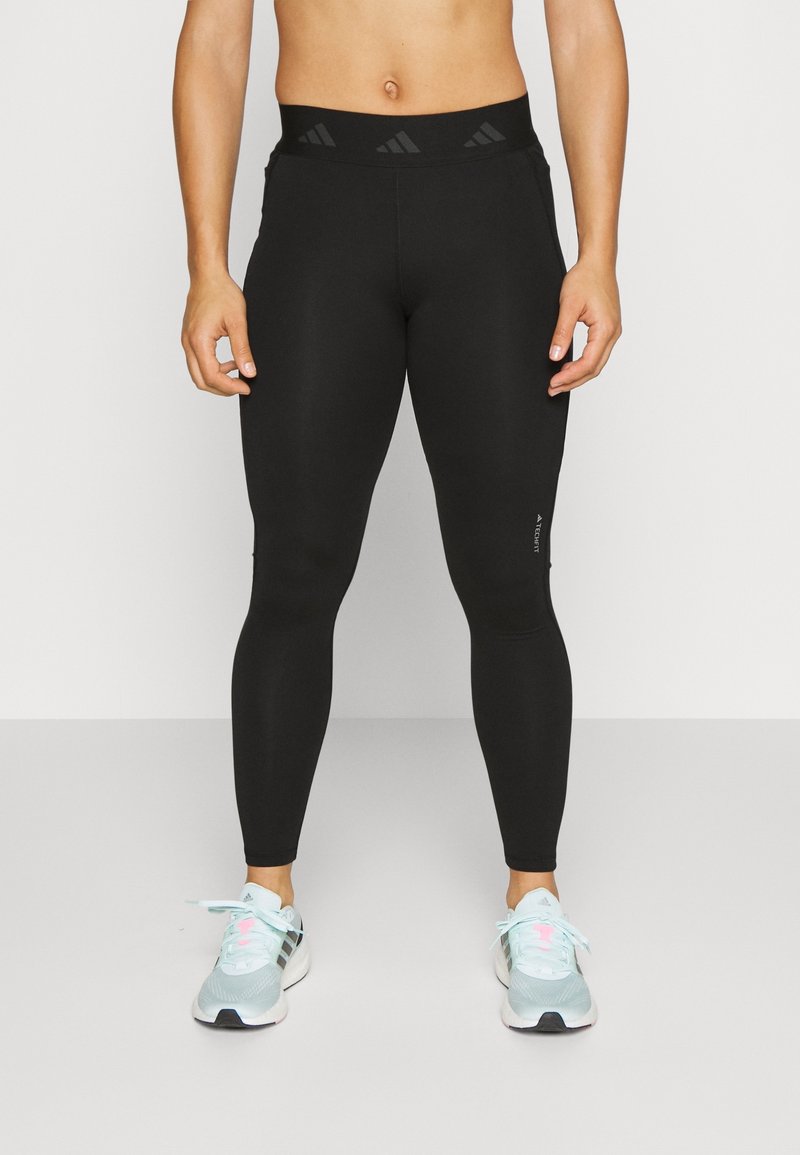 Leggings negros con una cintura alta que presentan acentos texturizados y un ajuste elegante. Llevadas con zapatillas deportivas de color azul claro.
