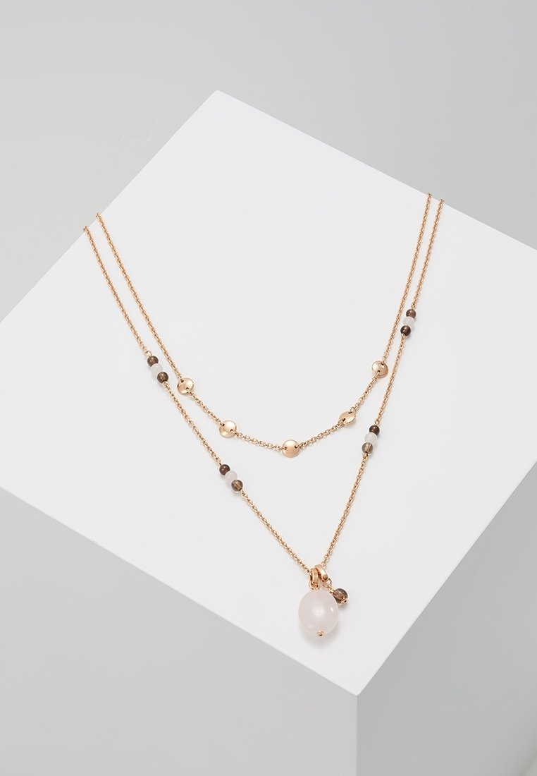 Collier délicat à double chaîne en or avec de petites perles et un pendentif en pierre ovale rose sur une surface angulaire blanche.