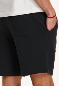 Schwarze Baumwollshorts mit lockerer Passform, ausgestattet mit seitlichen und einer Gesäßtasche. Der Bund ist elastisch für zusätzlichen Tragekomfort.