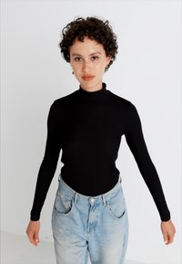 Juodas rins kaip kamuolys turtlenckas su ilgomis rankovėmis, derinamas su šviesiai mėlynomis aukšta juosmens džinsais. Audinys atrodo elastingas ir minkštas.