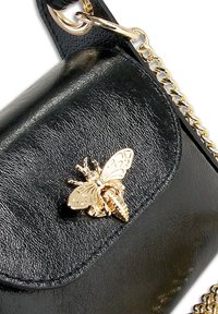 Schwarze Ledertasche mit goldener Bienenverzierung auf der Klappe, einem goldenen Kettenriemen und strukturierten Oberflächendetails.
