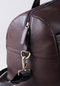 Brown leather bag with a textured surface, featuring a zipper closure, gold hardware, and a detachable black strap.