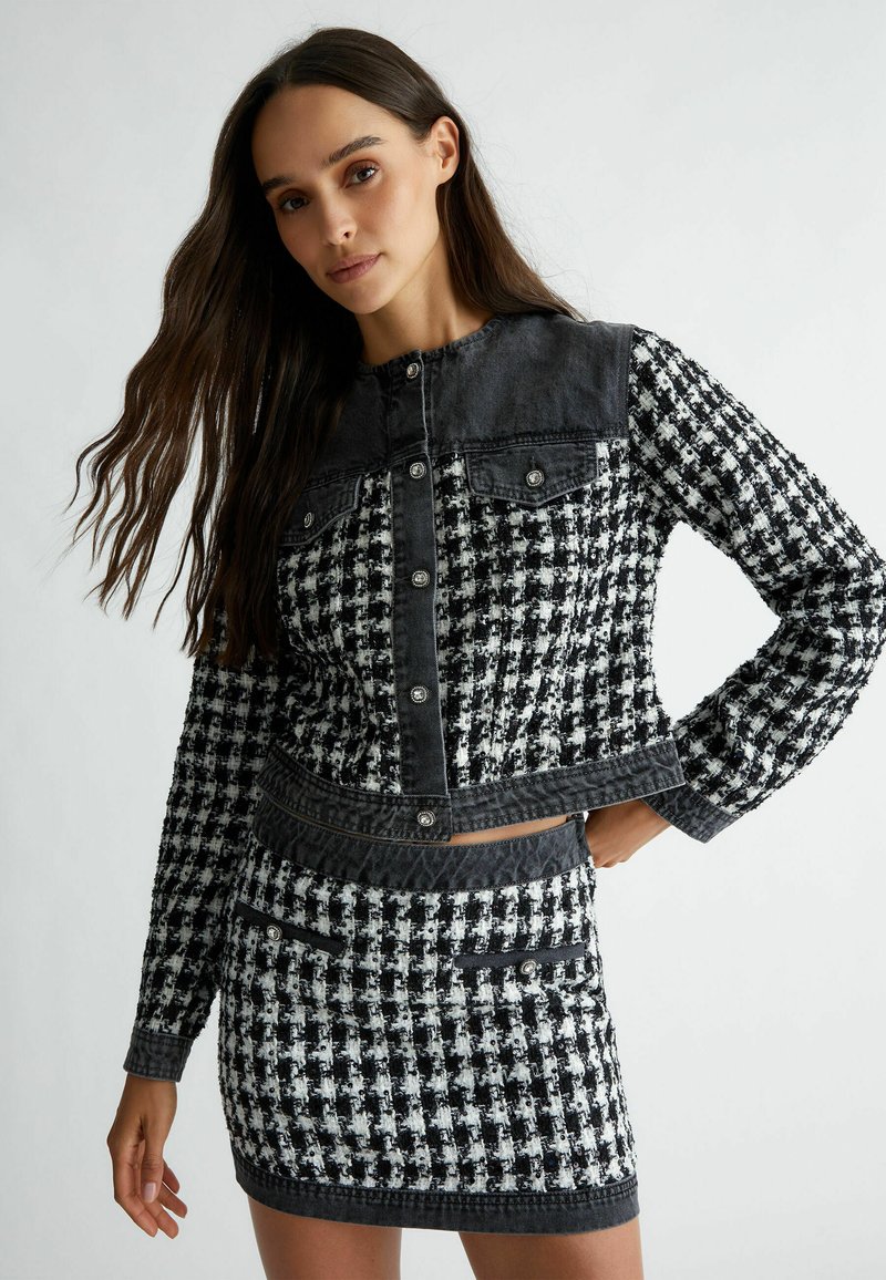Fekete-fehér hounds tooth mintás dzseki, denim kiegészítőkkel, patent gombokkal, két elülső zsebbel és cropped fazonnal. Tartalmaz egy illeszkedő szoknyát.