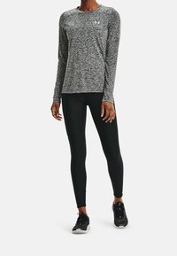 Langärmliges, graumeliertes Sportshirt mit Rundhalsausschnitt, kombiniert mit schwarzen Leggings und schwarzen Sportschuhen mit weißen Akzenten.