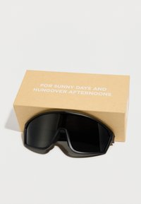 Μαύρα wraparound γυαλιά ηλίου που στηρίζονται σε μια καφέ θήκη με το κείμενο «Για ηλιόλουστες μέρες και μεθυσμένα απογεύματα.»