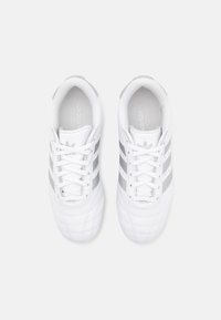 White athletic shoes with synthetic leather material, featuring three gray stripes, lace-up design, and raised stitching details.