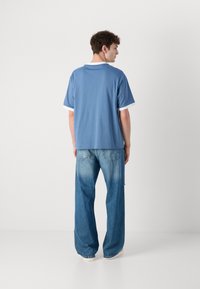 Light blue short-sleeve t-shirt with white trim, paired with loose-fitting, faded blue jeans and light-colored shoes, viewed from behind.