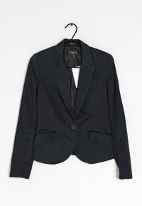 Blazer blu scuro con rever a taglio, chiusura a un bottone, due tasche frontali e un tessuto liscio. Appeso a un gancio nero.