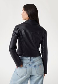 Black faux leather cropped jacket with a collar, smooth texture, and seam detailing, paired with light blue high-waisted jeans.